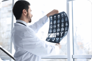A imagem mostra um médico, de jaleco branco, em um ambiente bem iluminado (provavelmente um consultório ou clínica, com uma grande janela ao fundo), olhando atentamente para uma folha de exame de imagem. A folha, que parece ser uma chapa de ressonância magnética ou tomografia, exibe múltiplas "fatias" ou cortes axiais do cérebro. O médico está de costas ou de perfil, segurando o filme contra a luz para melhor visualização.