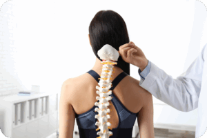 Fisioterapeuta examinando a coluna vertebral de uma paciente usando um modelo anatômico da coluna (espinha dorsal). A paciente está de costas, e o profissional, de jaleco branco, aponta para o modelo, demonstrando o alinhamento ou a estrutura óssea.